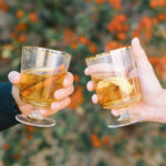 Two hands holding hot toddies getting ready to clink glasses.