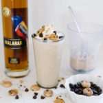 A Kahlua Malabar Milkshake garnished with cookies and marshmallows next to a bottle of Malabar.