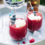 Two Red Berry Sangria Slush cocktails on a white tray with berries in a bowl.
