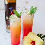 Two Spiced Tropical Sunrise next to a bottle of Malabar Spiced Liqueur.