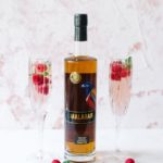 Two glasses of Malarose with rasberries and a bottle of Malabar Spiced Liqueur.