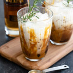 Two Malabar Salted Caramel White Russian cocktails in tall glasses next to a bottle of Malabar Spiced Liqueur.