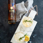 Two Malabar Lemon Honey Gin And Tonics on a marble slab next to a bottle of Malabar Spiced Liqueur.