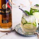 Two Malabar Cucumber Refreshers in short glasses garnished with mint next to a bottle of Malabar Spiced Liqueur.